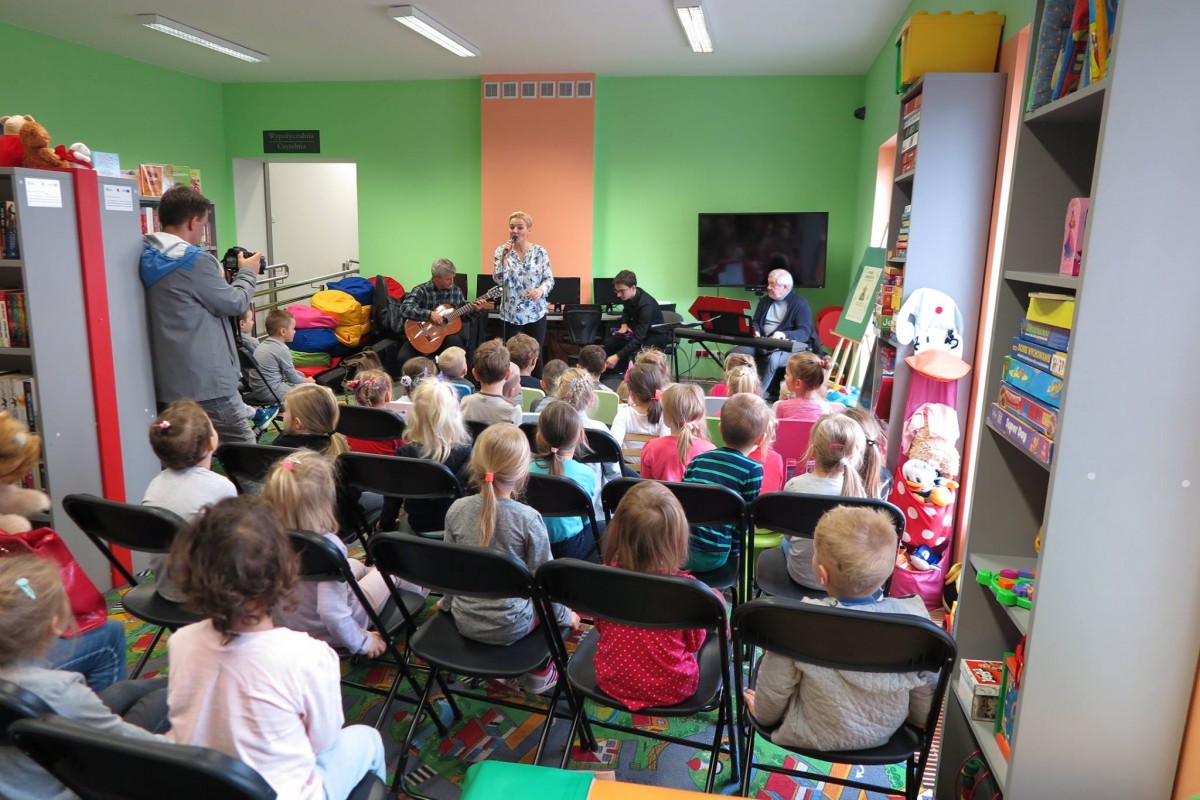 Wnętrze biblioteki, na krzesełkach siedzą dzieci z grupy II i III z Przedszkola nr 3 słuchają koncertu Kasi Sobczyk. 