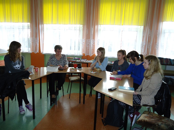 Wnętrze biblioteki w gimnazjum nr 2 w Działdowie, przy stolikach siedzą członkinie DKK GIM NR 2 wspólnie omawiają  książkę J. Brown "Nienawiść".