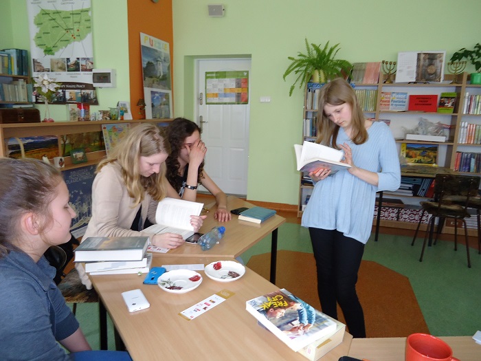 Wnętrze biblioteki w gimnazjum nr 2 w Działdowie, przy stolikach siedzą członkinie DKK GIM NR 2 wspólnie omawiają  książkę J. Brown "Nienawiść".