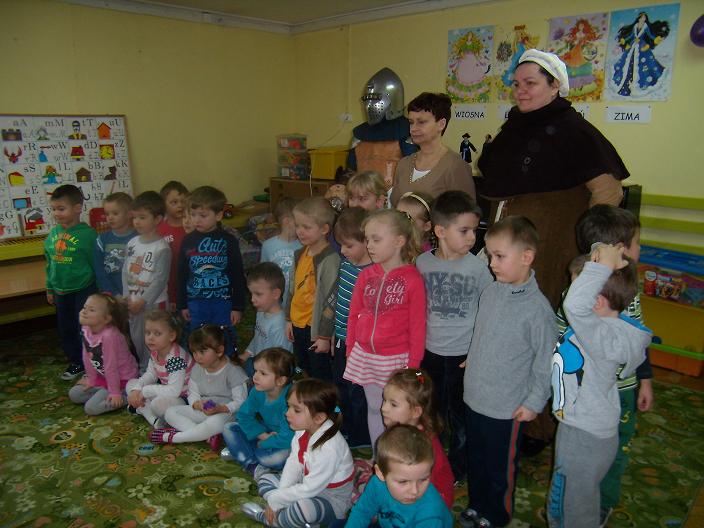 Wnętrze przedszkola, grupa dzieci z opiekunkami i rycerzem z Bractwa Rycerskiego.