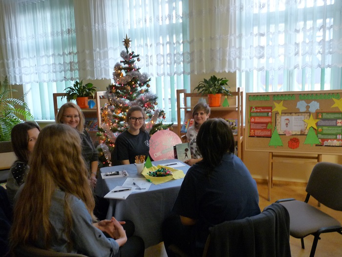 Przy stoliku siedzą uczestnicy DKK GIM NR 1 wspólnie omawiają  książkę F. Moccia "Trzy metry nad niebem" za nimi stoi choinka świąteczna.