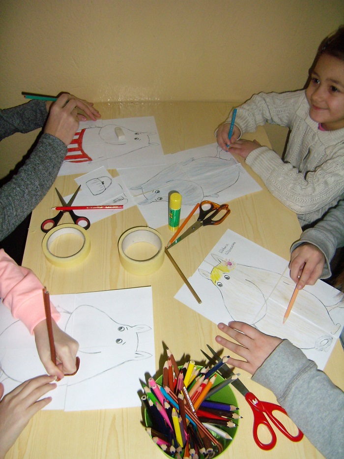 Przy stoliku siedzi czworo dzieci razem kolorują muminki.