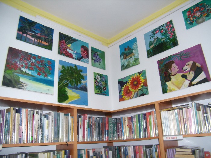 Wnętrze biblioteki, nad regałem z książkami wisi wystawa prac Krystyny Etzrodt Kozłowskiej.