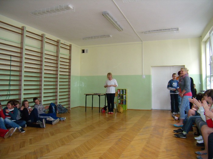 Wnętrze sali gimnastycznej przy drewnianych drabinkach siedzi grupa dzieci w oddali  nauczyciele i autorka książek dla dzieci Beata Ostrowicka.