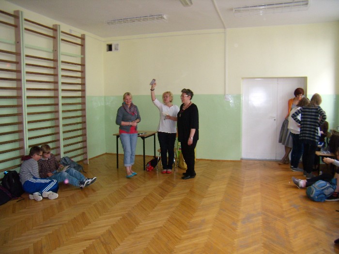 Wnętrze sali gimnastycznej przy drewnianych drabinkach siedzi grupa dzieci w oddali  nauczyciele i autorka książek dla dzieci Beata Ostrowicka.