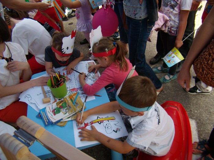 Rynek miasta Działdowa, festyn ''Wstąp po zdrowie'' przy niebieskim stoliku siedzą dzieci wykonują prace plastyczne.