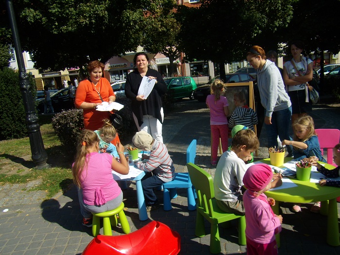 Przy stolikach siedzą dzieci wspólnie wykonują prace plastyczne.
