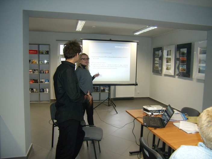Wnętrze biblioteki, dwóch prowadzących szkolenie z ochrony danych osobowych, w tle prezentacja multimedialna.