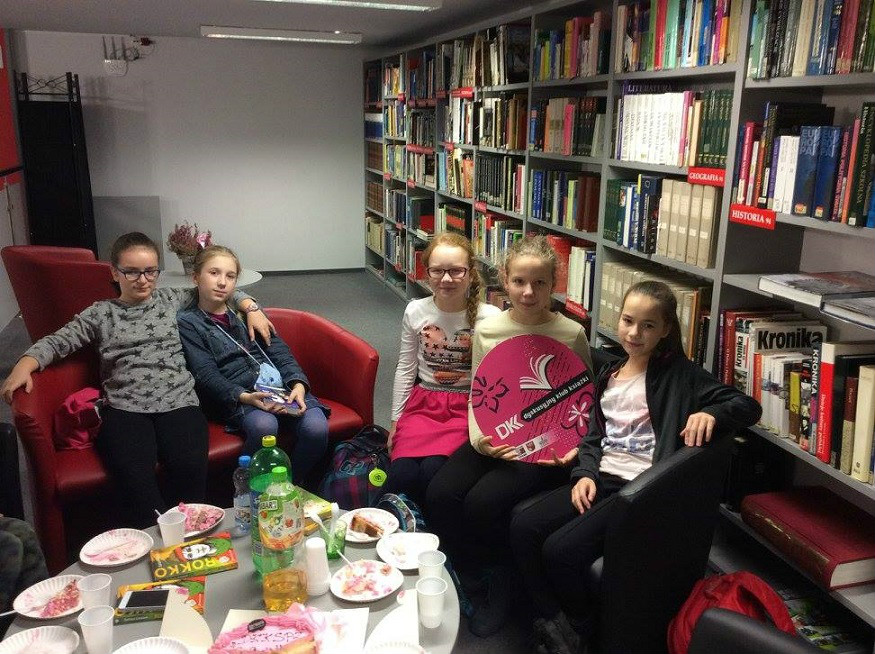 Wnętrze biblioteki. Grupa młodzieży z DKK SP 3 wspólnie omawiają książkę Barbary Ciwoniuk "Rokko".