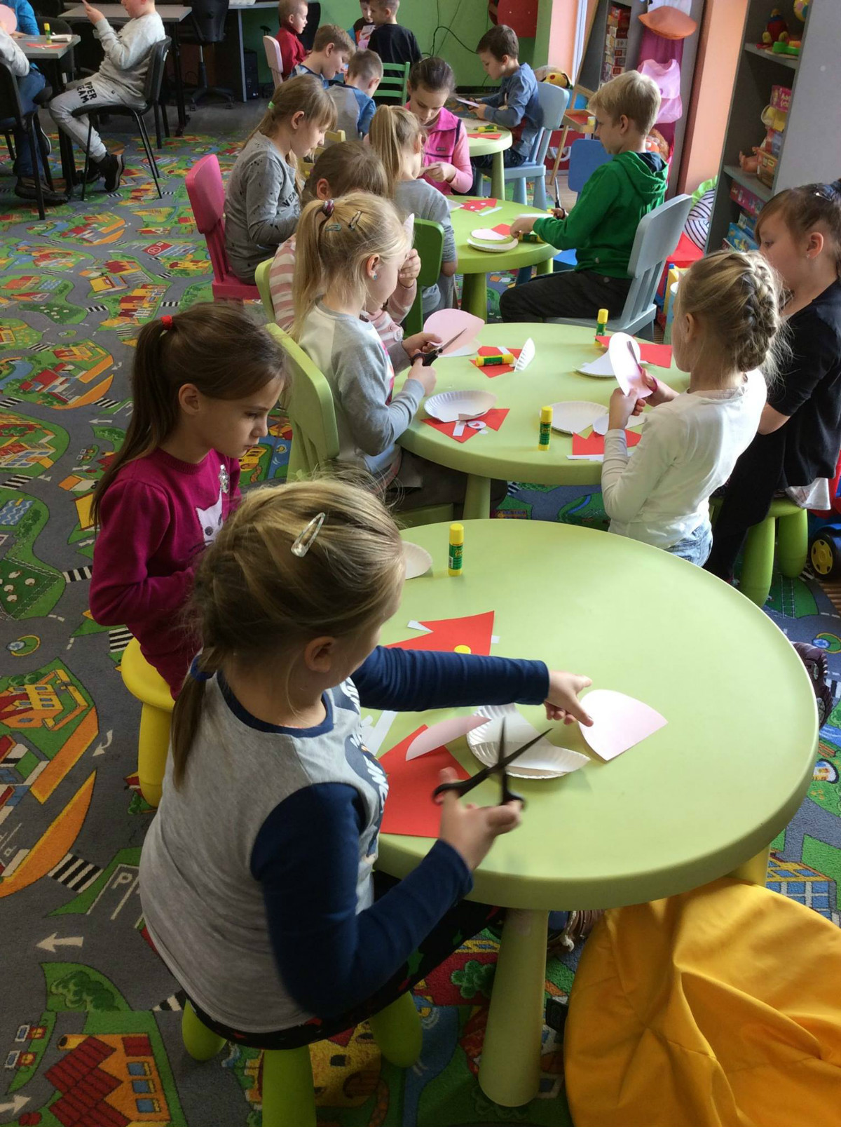 Przy stolikach siedzą dzieci wspólnie wykonują Mikołaja z talerzyka papierowego.