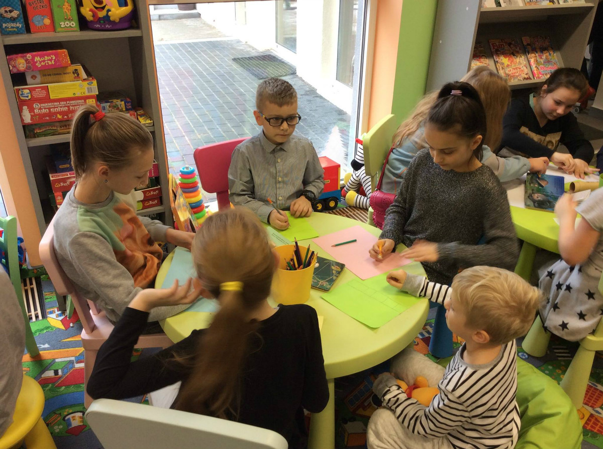 Grupa dzieci przy stoliku wykonuje prace plastyczne.