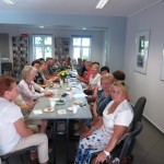Wnętrze biblioteki. Przy stolikach siedzą uczestnicy DKK UTW wspólnie omawiają książkę pt „Zapach świeżych malin” autorstwa Krystyny Wasilkowskiej-Frelichowskiej.