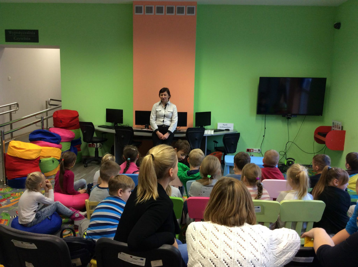 Wnętrze biblioteki. Na krzesełkach siedzą dzieci ze SP NR 3 biorą udział w zajęciach edukacyjnych. 