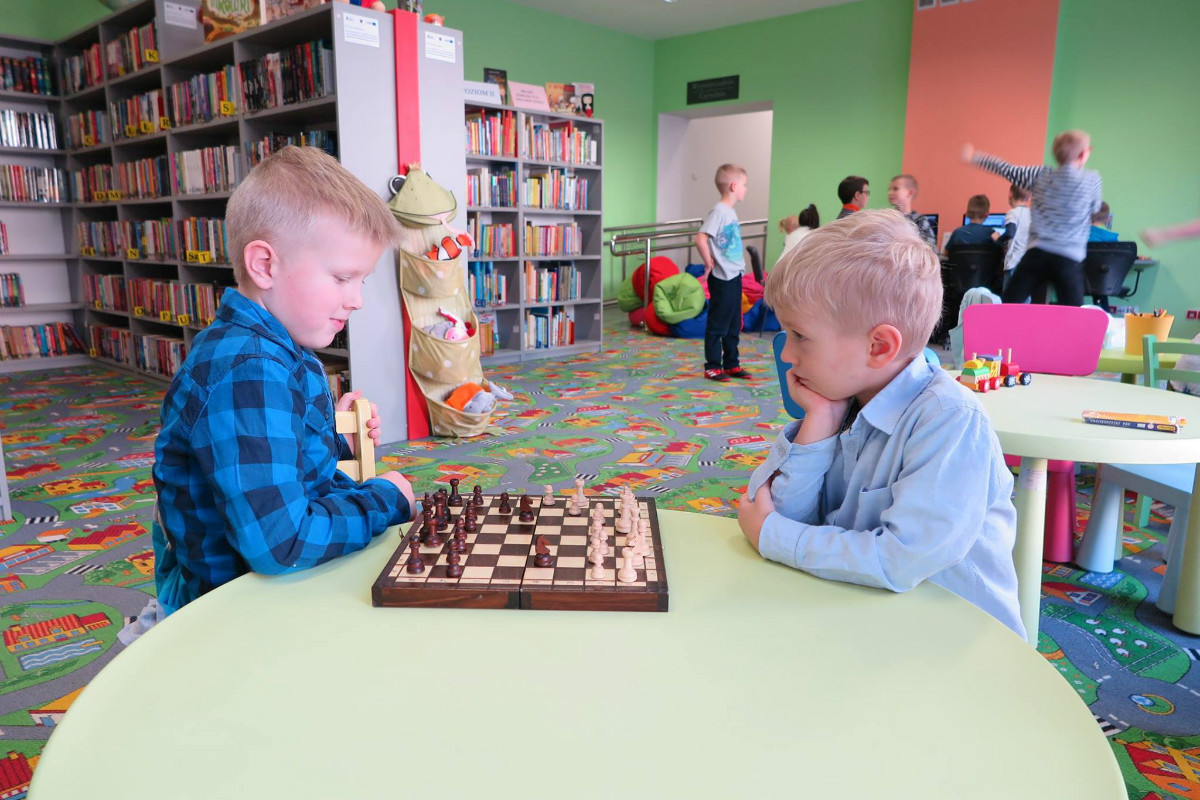 Przy stoliku siedzi dwóch chłopców, grają razem w szachy.