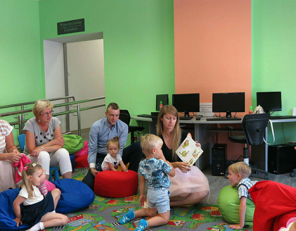 Wnętrze biblioteki. Dzieci wraz z opiekunami słuchają  opowiadania o Franklinie, który idzie do szkoły, czyta bibliotekarka Ola Cybulska.