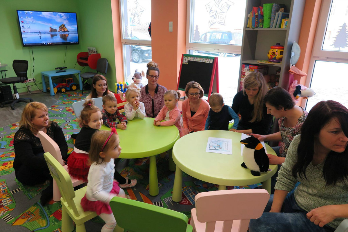 Przy stolikach siedzą dzieci z opiekunami, bibliotekarka Ania czyta  "Bajkę o pingwinim jaju" A. Galicy. 
