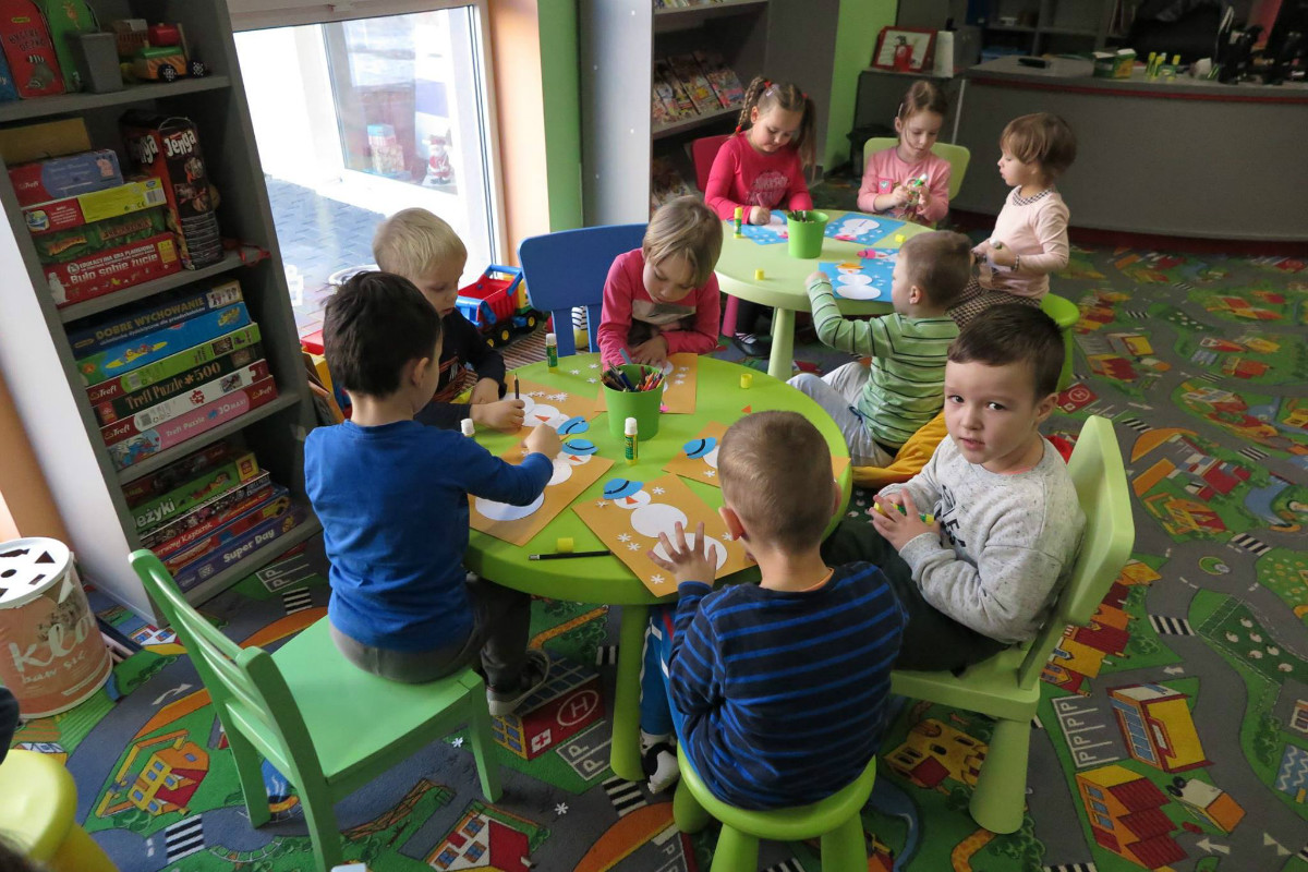 Przy stolikach siedzą dzieci razem wykonują prace plastyczne.