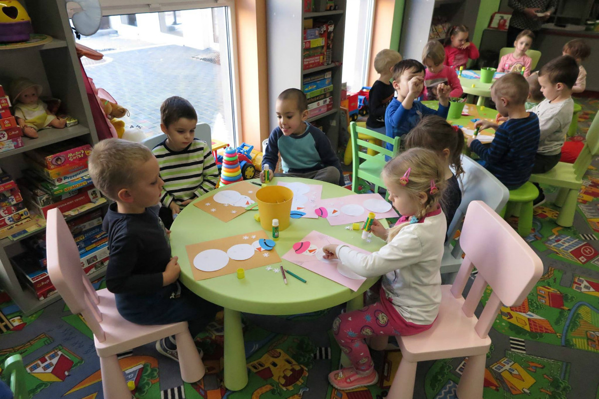 Przy stolikach siedzą dzieci razem wykonują prace plastyczne.
