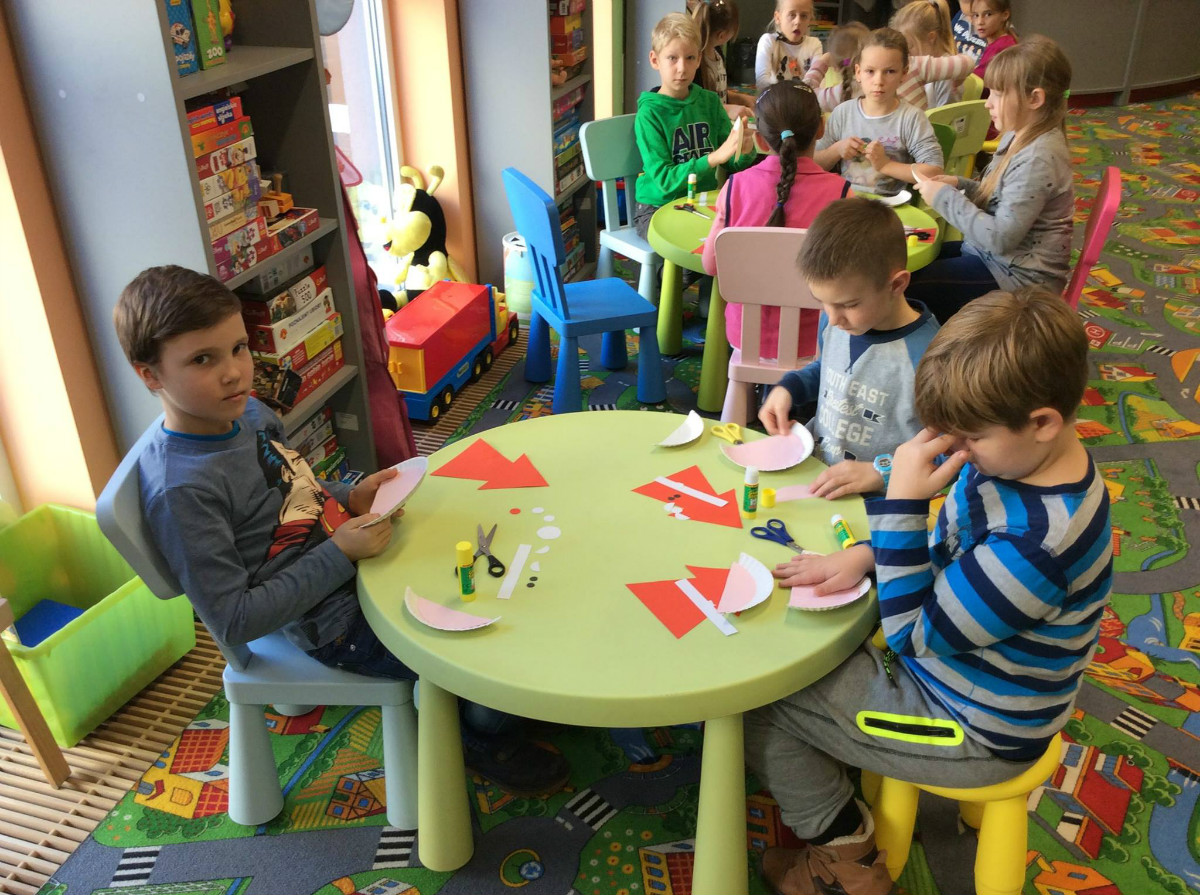 Przy stolikach siedzą dzieci wspólnie wykonują Mikołaja z talerzyka papierowego.