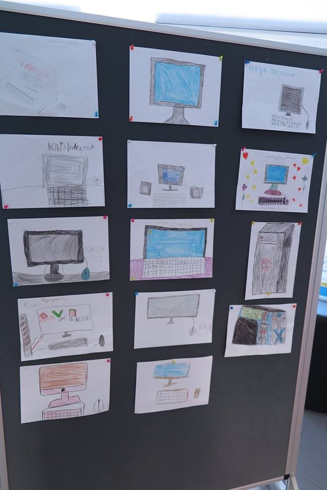 Na banerze wisi 14 prac plastycznych dzieci przedstawiające komputery.