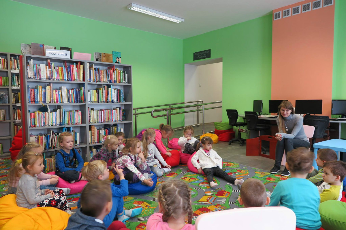 Wnętrze biblioteki, na pufach siedzą dzieci, bibliotekarka Aleksandra Cybulska prowadzi z nimi zajęcia na temat najważniejszych wartości.