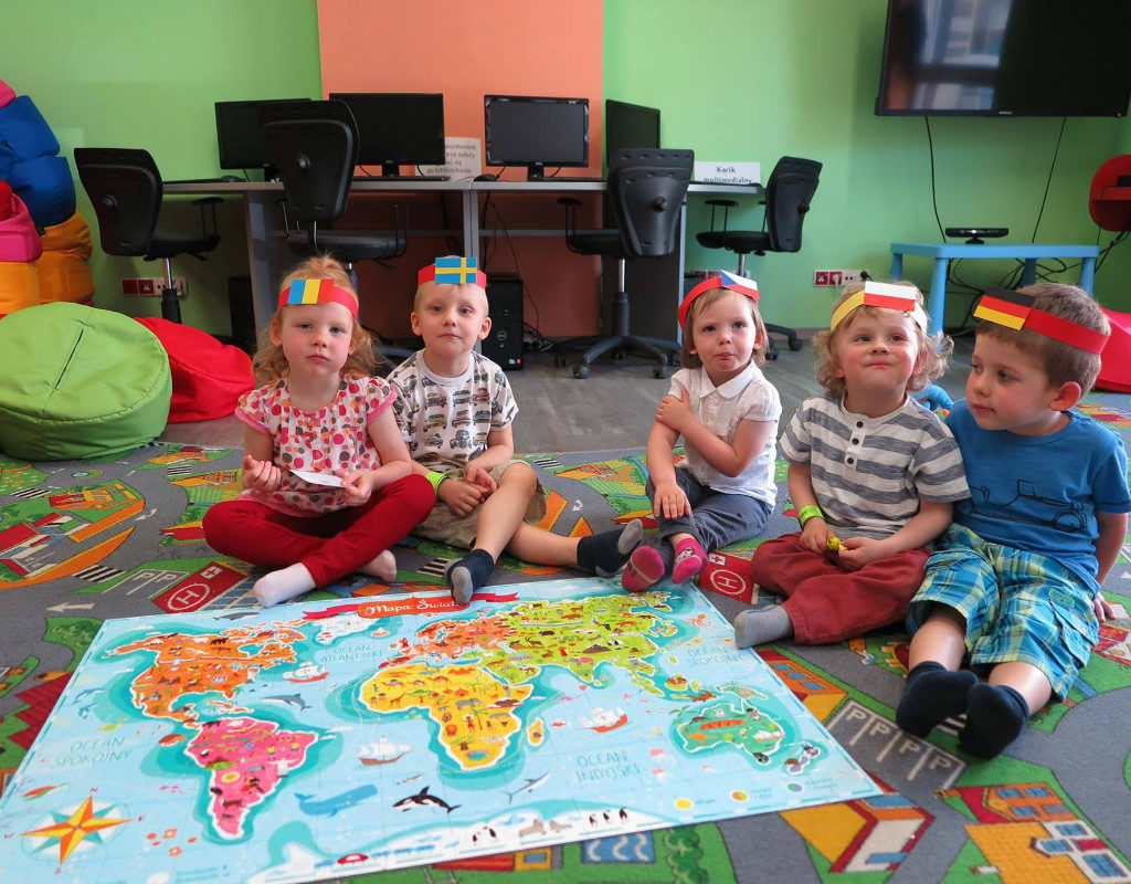 Dzieci z opaskami róznych państw siedzą przy mapie świata.