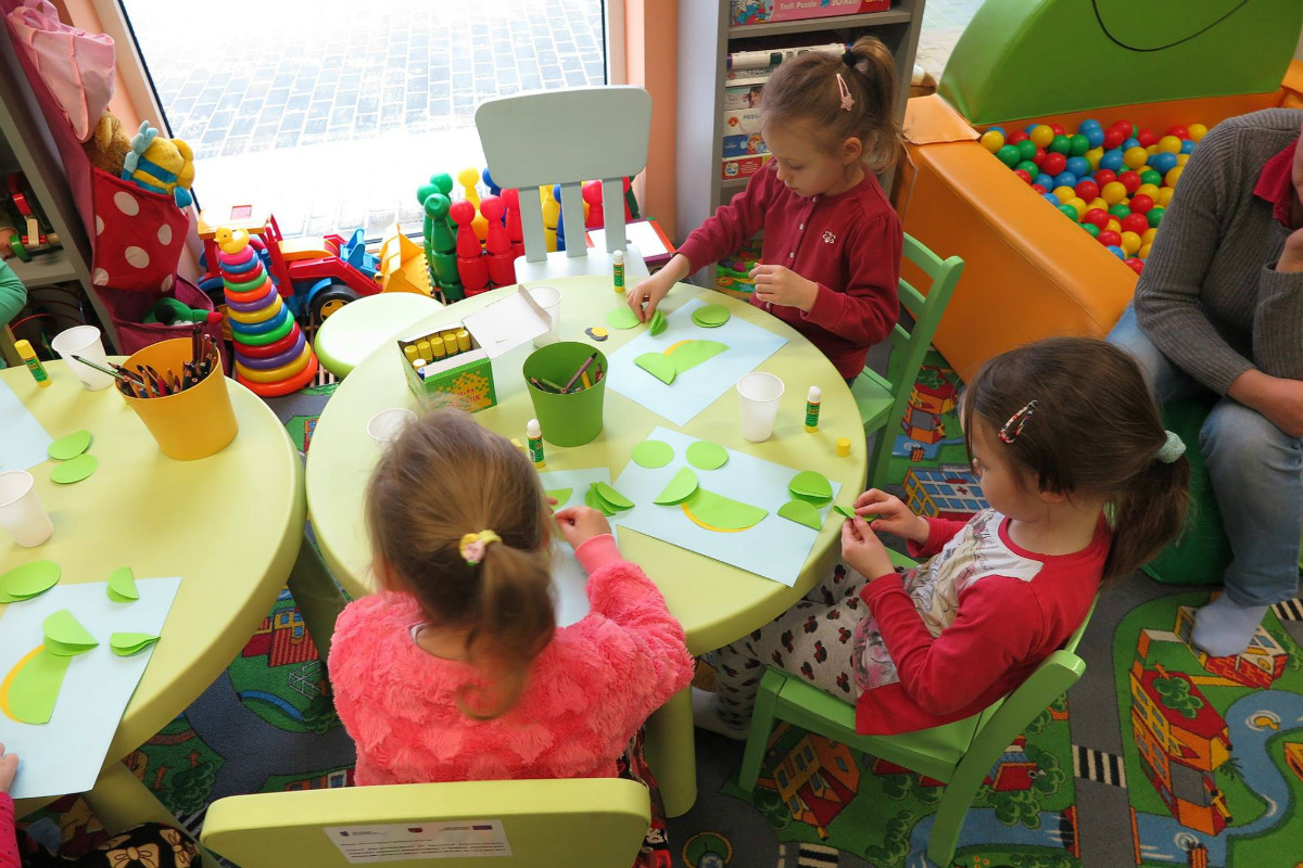 Przy stoliku siedzą dzieci wykonują smoki z wcześniej przygotowanych elementów.