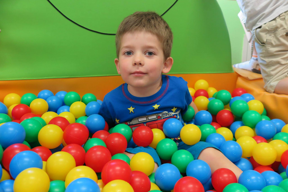 Chłopiec siedzi w basenie z kolorowymi piłeczkami.
