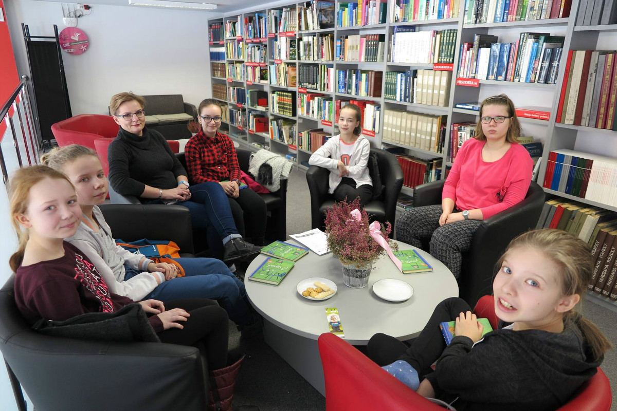 Wnętrze biblioteki, przy stoliku siedzą uczestniczki klubu DKK SP 3, wspólnie omawiają książkę "Samotni.pl" Barbary Kosmowskiej.