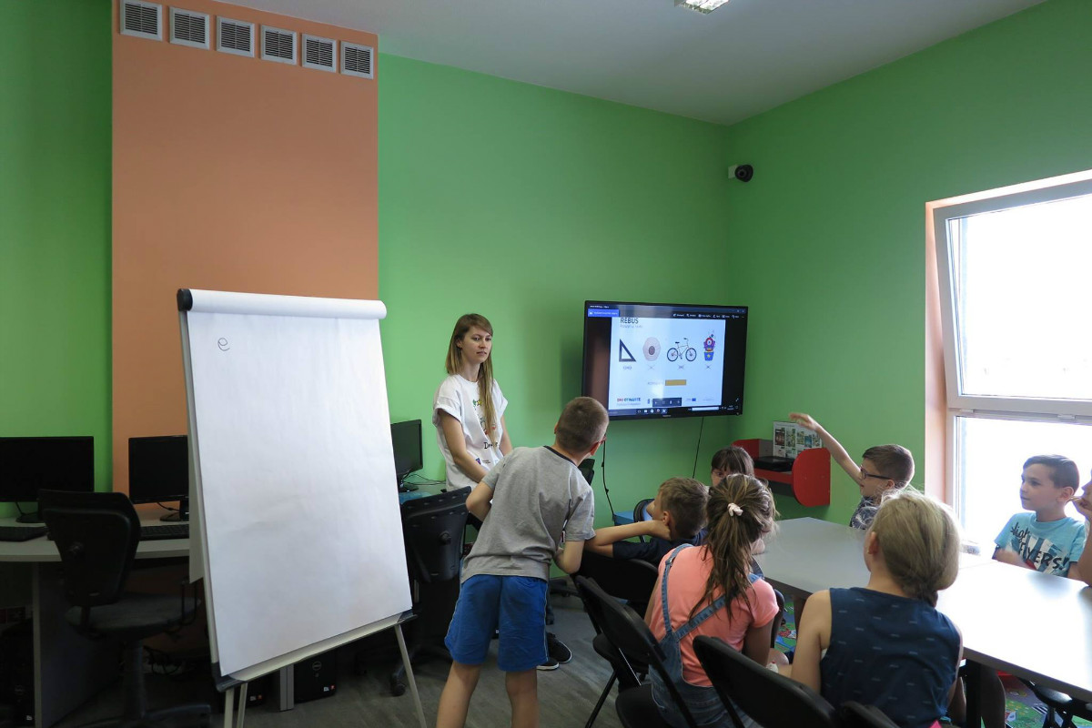 Wnętrze biblioteki. Grupa dzieci razem z bibliotekarką Aleksandrą Cybulską ogląda prezentację o unii europejskiej. 