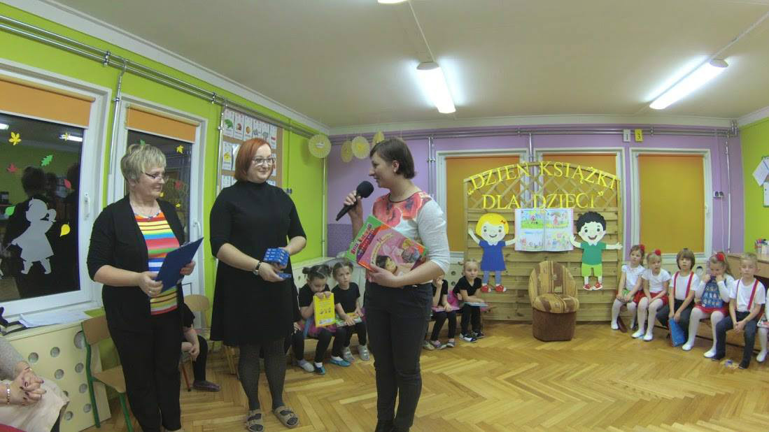 Wnętrze Przedszkola nr 4 dzieci uczestniczą w spotkaniu pod hasłem "Dzień książki dla dzieci". Przy mikrofonie bibliotekarka Ania Wiśniewska.