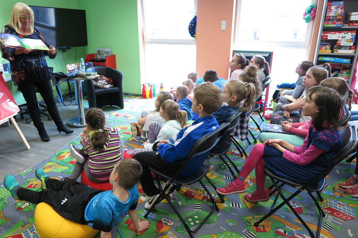 Na krzesełkach siedzą dzieci biorą udział w zajęciach z autorką książek dla dzieci Agnieszką Frączek. 