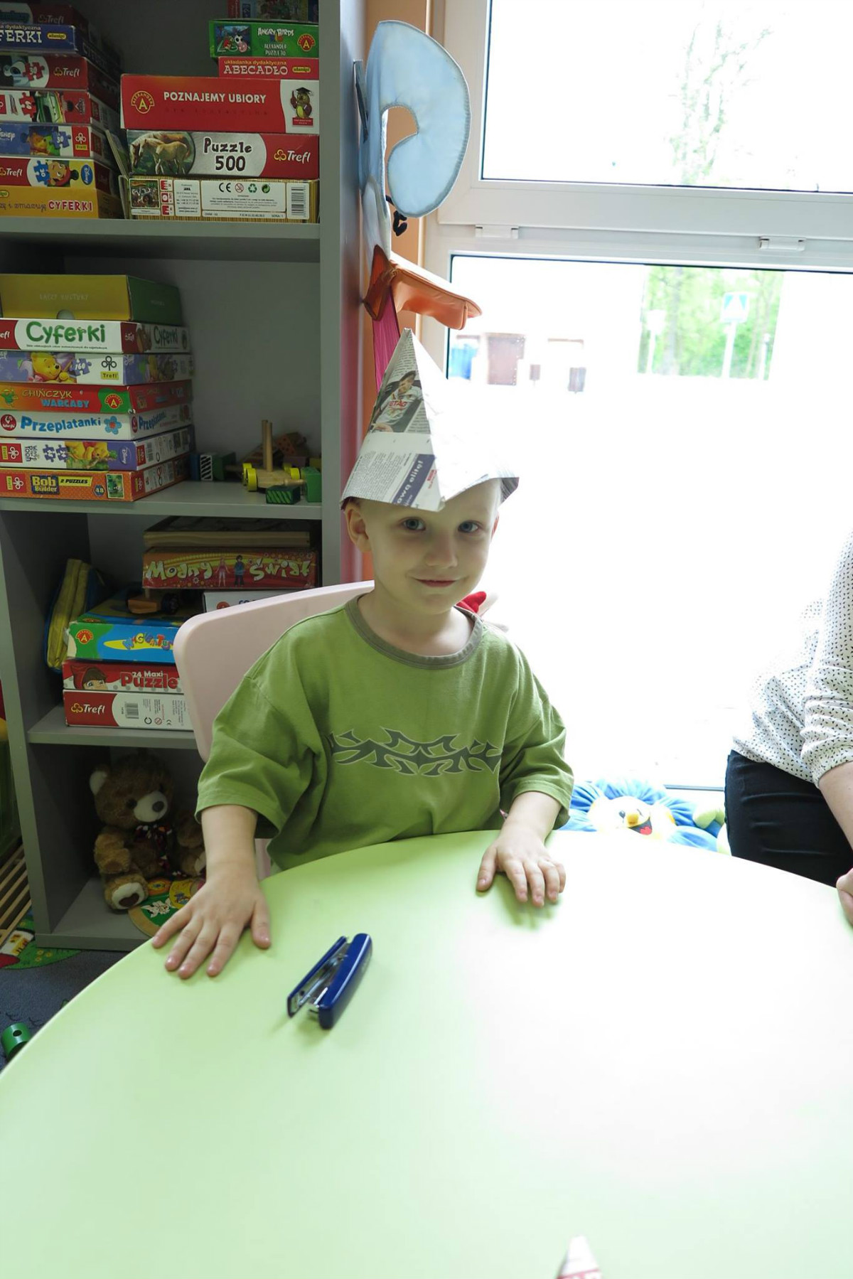 Przy stoliku siedzi chłopiec z papierową czapką na głowie.