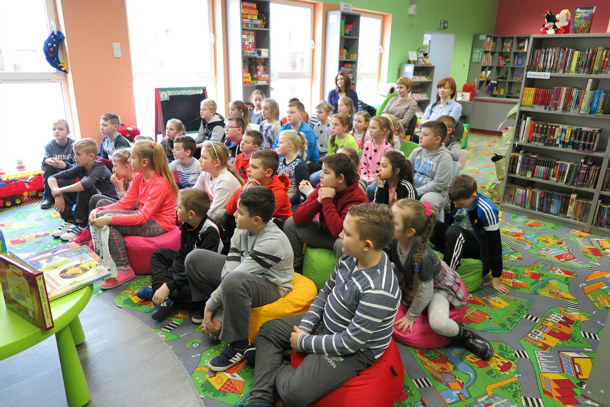 Wnętrze biblioteki. W oddziale dla dzieci uczniowie ze SP z Księżego Dworu biorą udział w lekcji bibliotecznej. 
