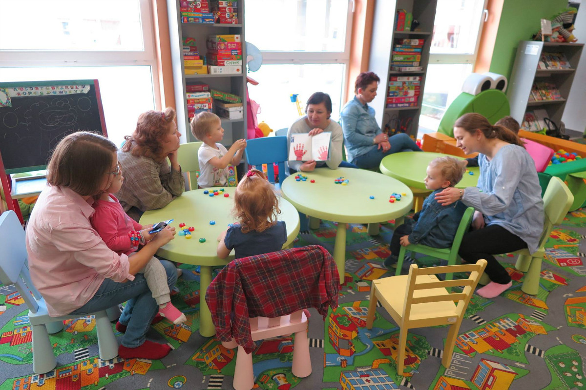 Wnętrze biblioteki, przy stoliku siedzą dzieci bibliotekarka Ania Wiśniewska czyta dzieciom wiersze Marcina Brykczyńskiego z książki "Liczydełko".