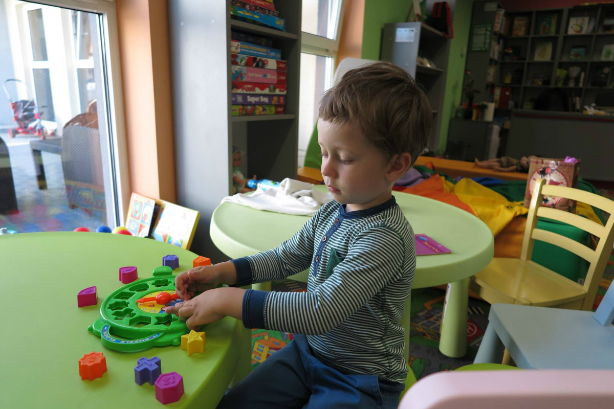Przy stoliku chłopiec układa kolorowe klocki. 