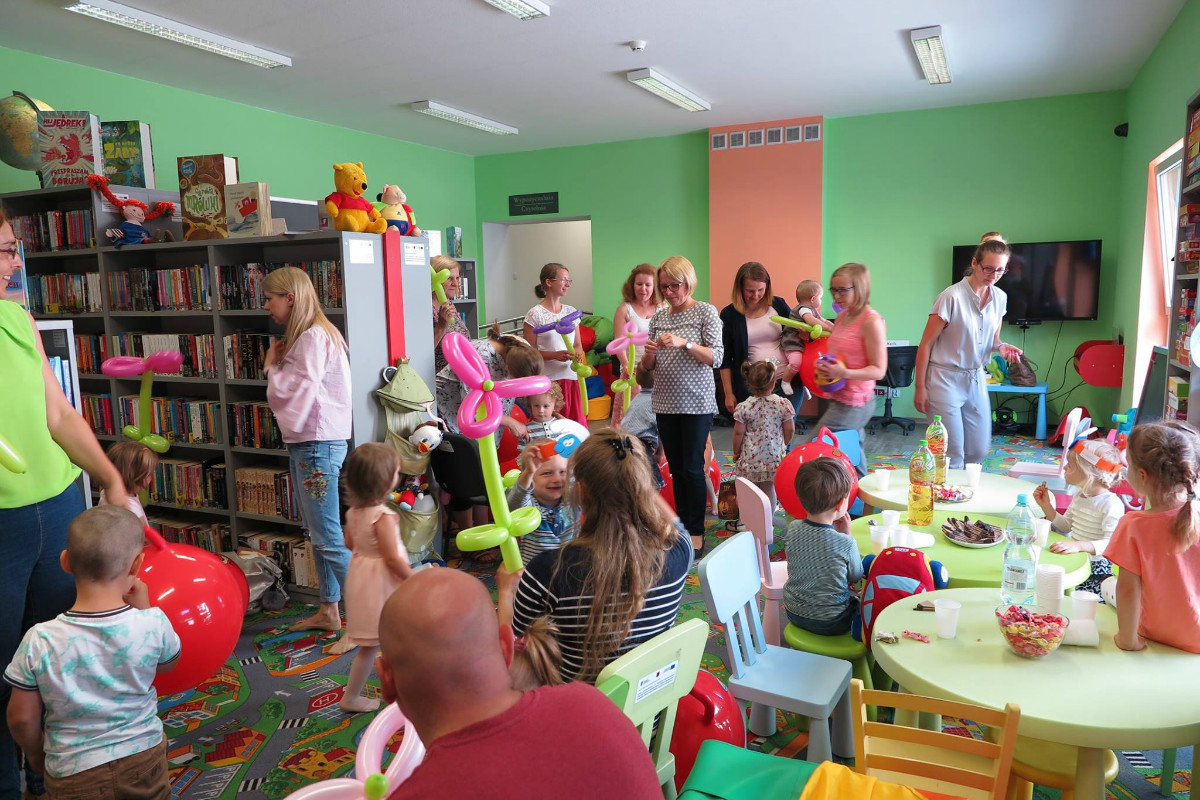 Wnętrze biblioteki. Grupa dzieci z opiekunami podczas zakończenia roku w klubie malucha.