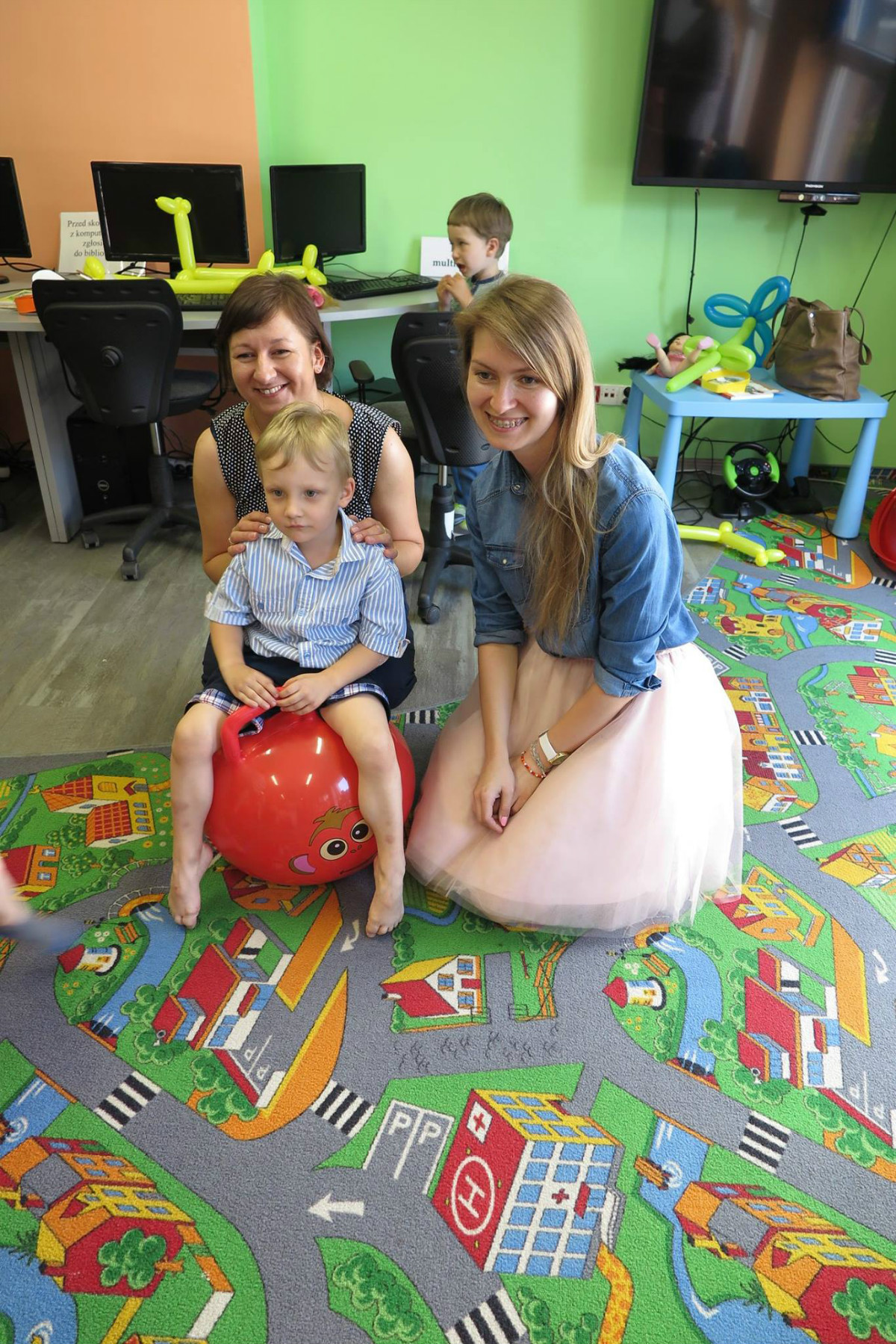Na czerwonej piłce siedzi chłopiec obok bibliotekarki Ola Cybulska i Ania Wiśniewska.
