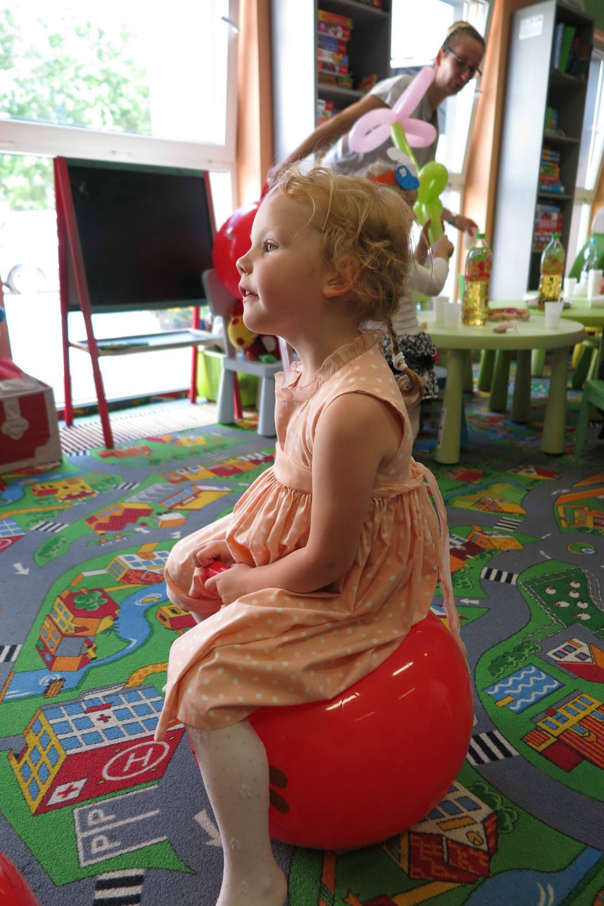 Dziewczynka siedzi na czerwonej piłce podczas zakończenia roku w klubie malucha. 