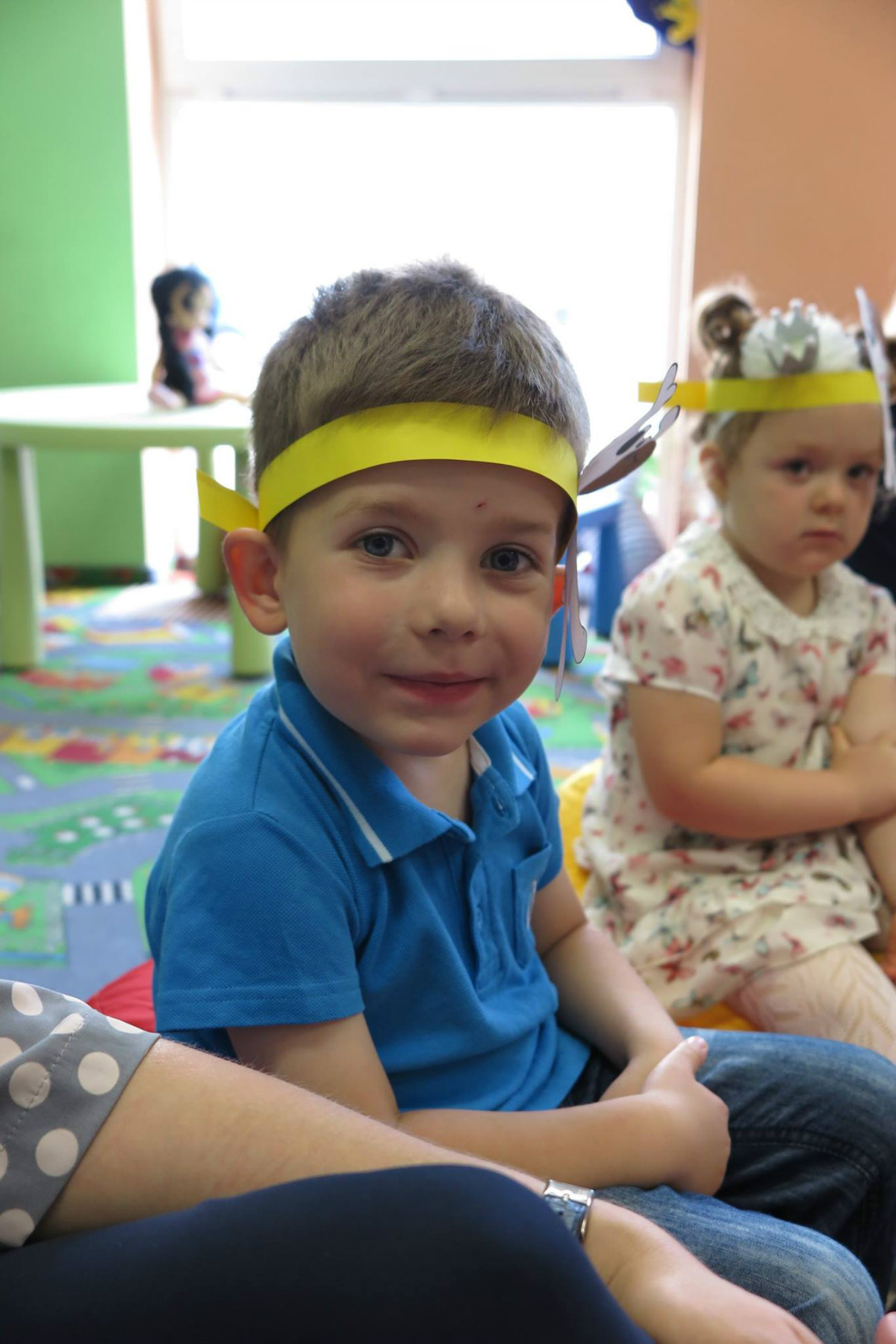 W oddziale dla dzieci na pufach siedzi chłopiec z dziewczynką w żółtych opaskach na głowie.