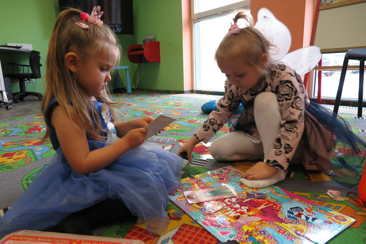 Dwie dziewczynki przebrane w kolorowe stroje grają w grę planszową w bibliotece.