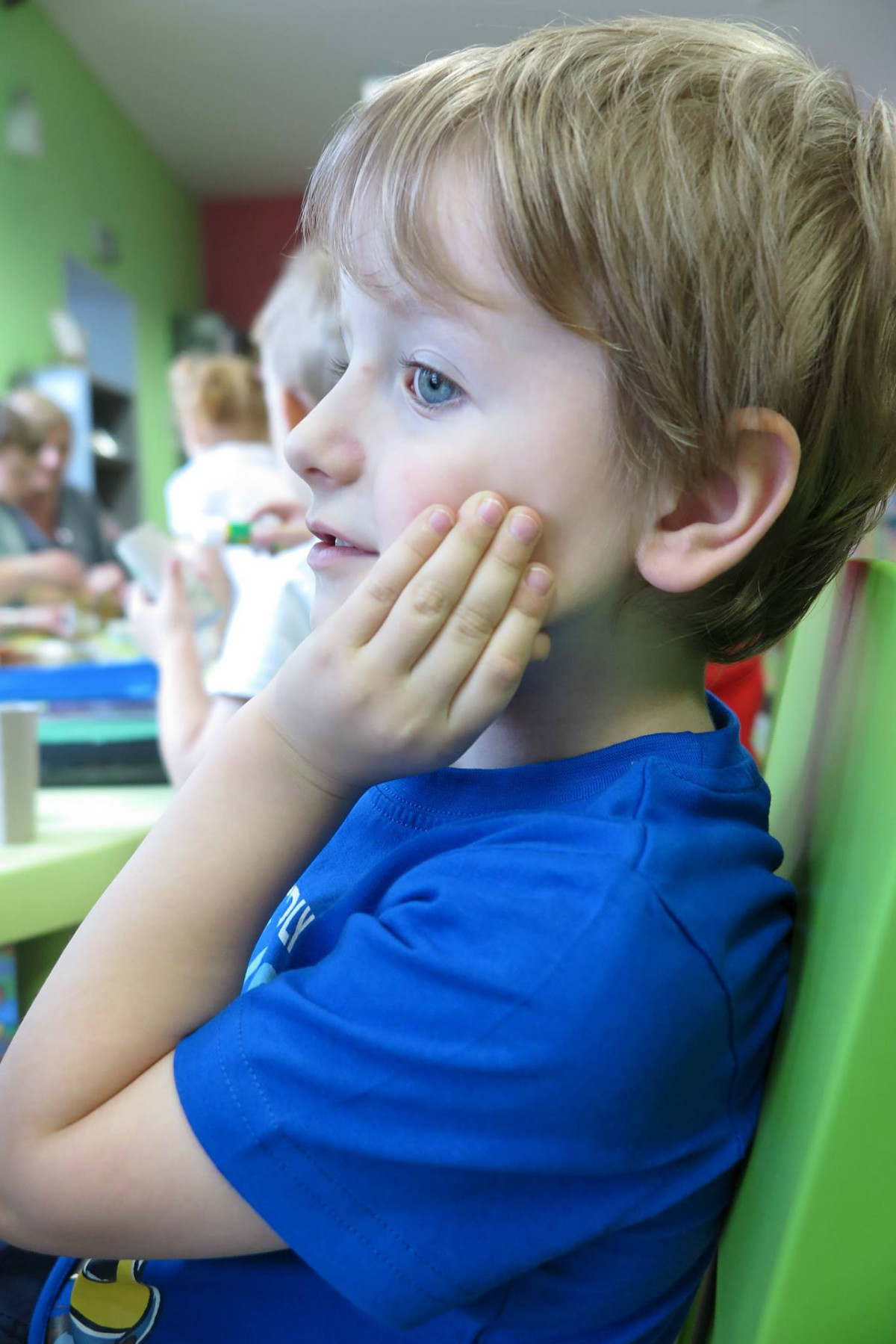Przy stoliku siedzi chłopiec w niebieskiej koszulce.