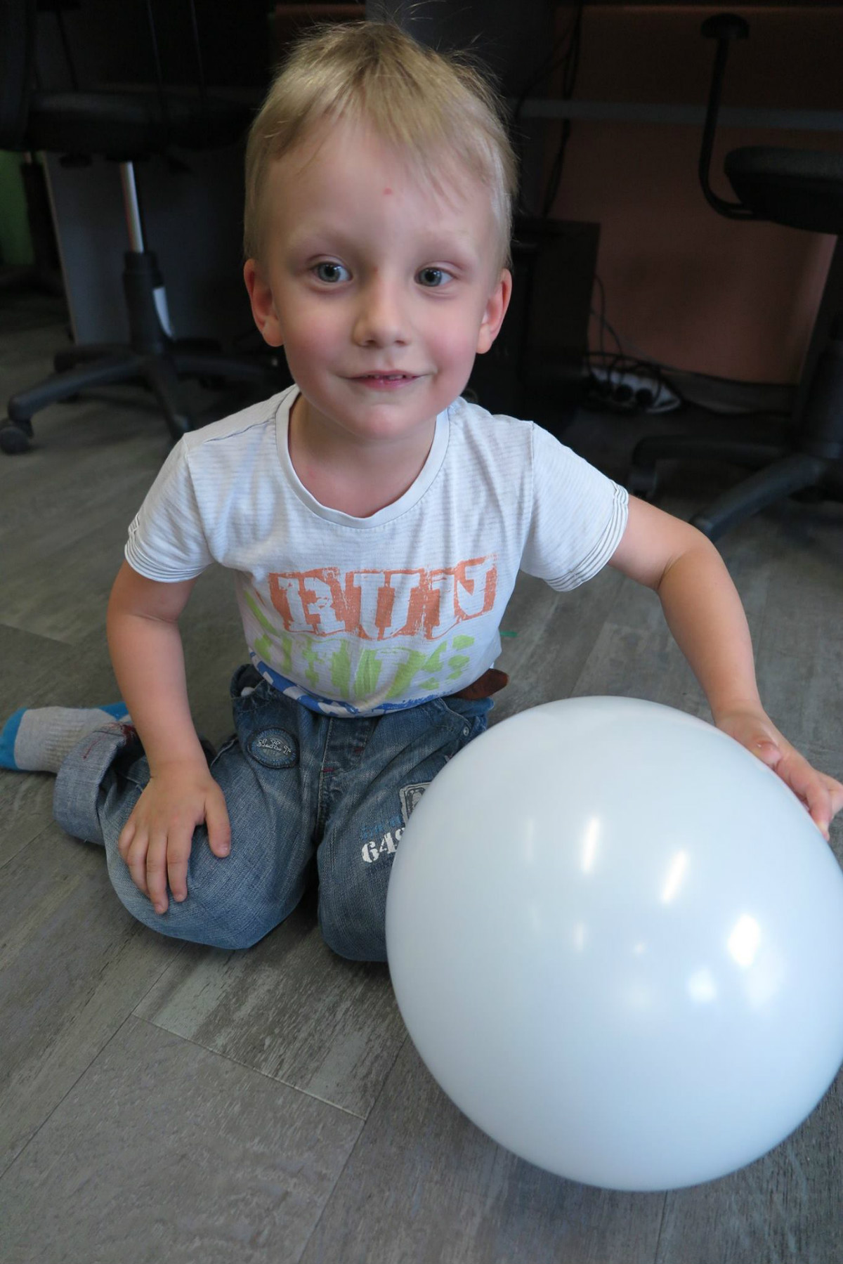 W oddziale dla dzieci siedzi chłopiec z białym balonem.