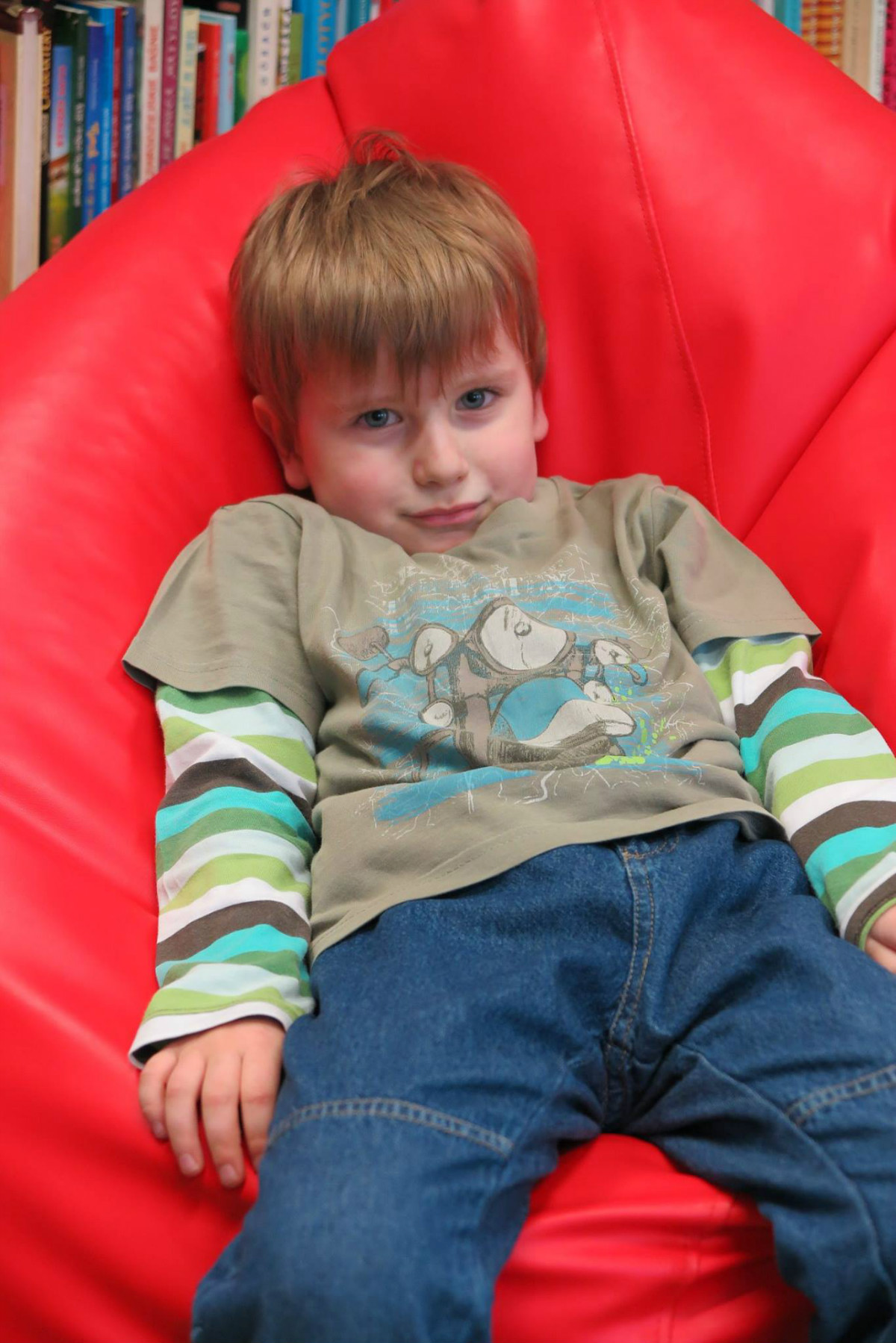 Chłopiec siedzi na czerwonej pufie w oddziale dla dzieci.