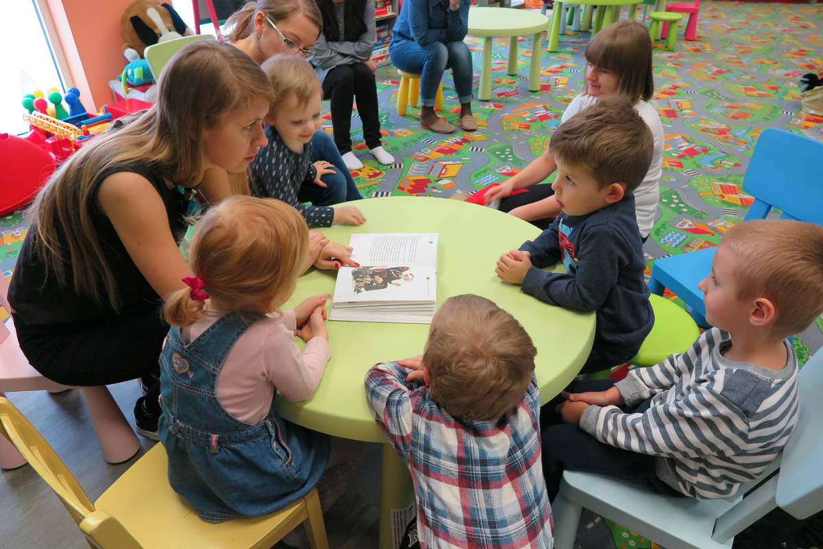 Przy stoliku siedzą dzieci z bibliotekarką Aleksandrą Cybulską.