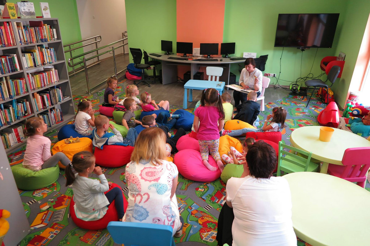 Wnętrze biblioteki. Na kolorowych pufach siedzą przedszkolaki z Narzymia. Słuchają teatrzyku paluszkowego "Czerwony Kapturek".