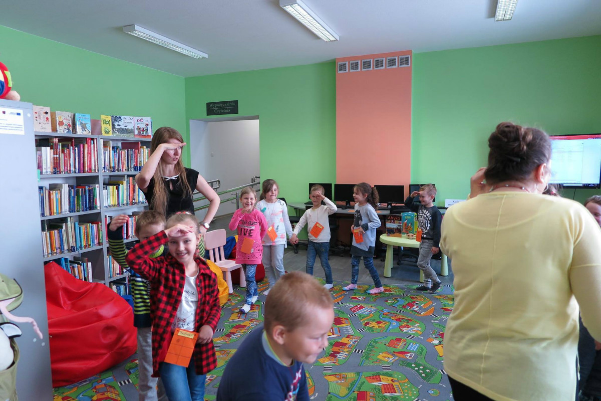 Grupa dzieci bawi się podczas zajęć w bibliotece. 