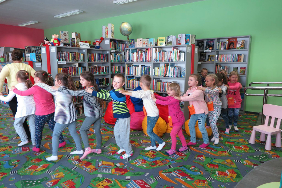Grupa dzieci bawi się podczas zajęć w bibliotece. 