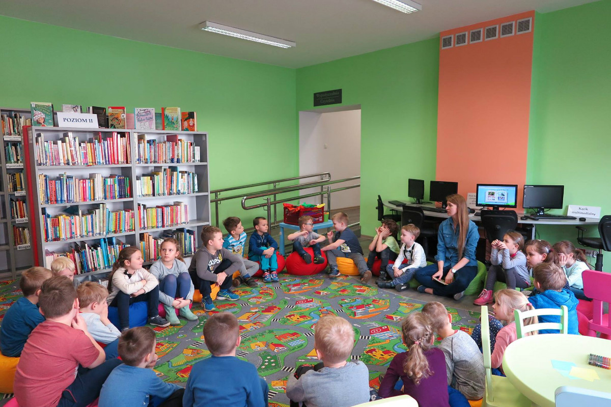 W oddziale dla dzieci siedzą w kole przedszkolaki, bibliotekarka Aleksandra Cybulska prowadzi zajęcia.