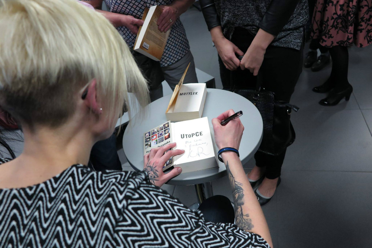 Przy stoliku autorka Katarzyna Puzyńska podpisuje książki czytelniczkom.